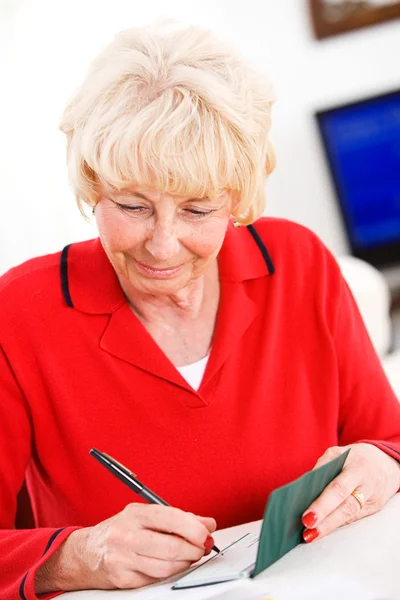 Seniors: Woman Cheerfully Writing Checks — Stock Photo, Image