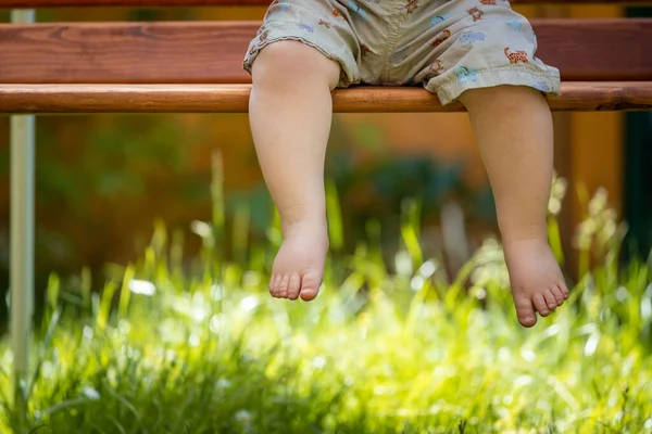 Baby grow up concept: Close up of barefoot baby feet sitting on park bench, summer time