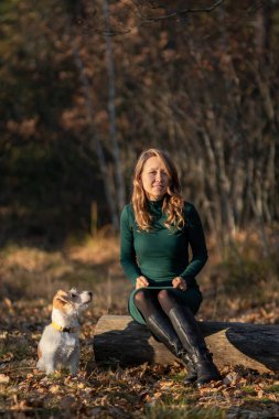 Tel saçlı Jack Russell Terrier köpeğinin portresi ve sonbahar parkında yeşil elbiseli bir kız..