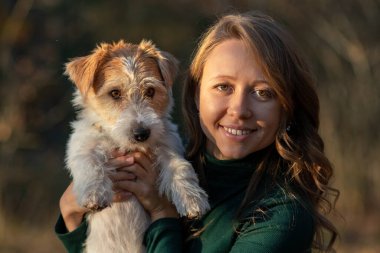 Tel saçlı Jack Russell Terrier köpeğinin portresi ve sonbahar parkında yeşil elbiseli bir kız..