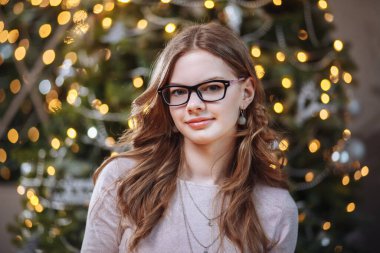 Yılbaşında bir ağacın arka planında gülümseyen bir kızın portresi.