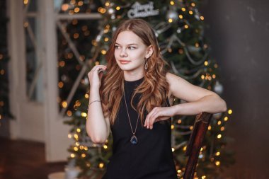 Siyah bir gece elbisesi giymiş çekici bir genç kızın portresi süslenmiş bir Noel ağacının arka planında..