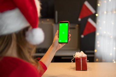Mutfakta kırmızı elbiseli bir kız elinde krom anahtarla akıllı telefonun ekranına bakıyor..