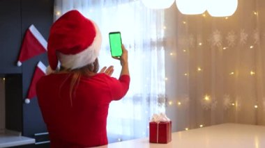 Mutfakta kırmızı takım elbiseli bir kız yeşil ekranlı bir akıllı telefondan parmağıyla yaprakları sarıyor.