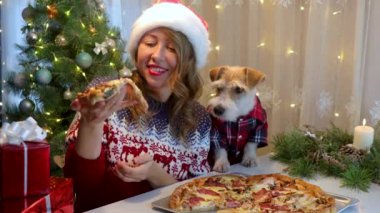 Masada şapkalı bir kız kırmızı gömlekli bir köpeğe pizza ikram ediyor. Noel 'den önce mutfakta akşam