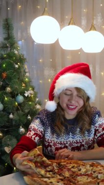 Kırmızı şapkalı bir kız, yeni yıl kutlamalarının arka planında pizza yiyor.