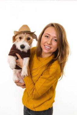 Sarı ceketli bir kız kovboy şapkalı bir Jack Russell Terrier köpeği tutuyor. Beyaz arkaplanda izole et.
