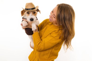Sarı ceketli bir kız kovboy şapkalı bir Jack Russell Terrier köpeği tutuyor. Beyaz arkaplanda izole et.