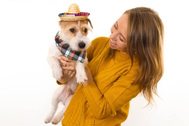 Sarı ceketli bir kız, şapkalı ve bandanalı bir Jack Russell Terrier köpeği tutuyor. Beyaz arkaplanda izole et.