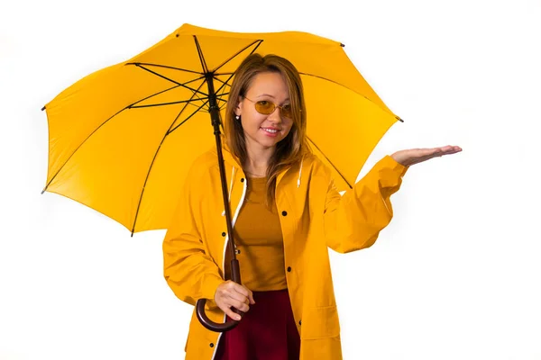 一个穿着黄色雨衣的微笑的女孩站在伞下 在雨中伸出手来 白色背景的分离 图库照片