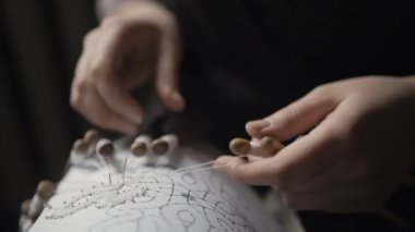 Female hands stick a needle into a stencil on paper and weave with bobbins