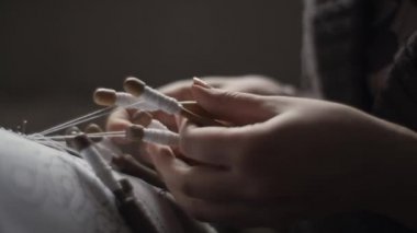 Female hands weaving and tightening lace threads with bobbins in a backlight