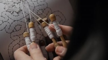 Detail close-up of female hands weaving lace with bobbins
