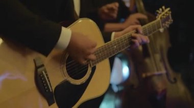Siyah takım elbiseli adam akustik gitar çalar.