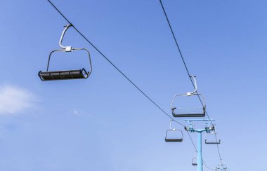 Empty chairs of ski lift against blue sky. Cable way of ski resort. Copy space