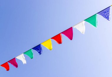 Mavi gökyüzü arka planında çok renkli üçgen bayraklar. Şenlik dekorasyonu. Boşluğu kopyala