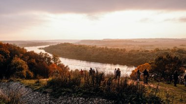 İnsanlar sonbaharda dağdaki gözlem güvertesinde durup nehre ve ormana bakarak gün batımını seyrediyorlar. Sonbahar güzel manzara.