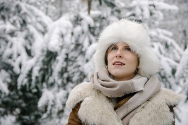 Koyun derisi ceketli, eldivenli, kulaklıklı ve çizmeli gülümseyen genç Avrupalı bir kızın yatay kış portresi.