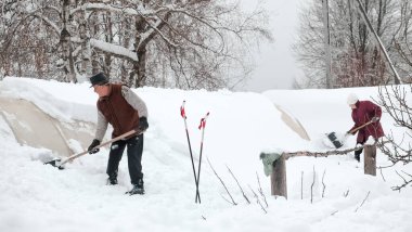 01.29.2022. Rusya, Tula, Skuratovo köyü. Yaşlı bir adam ve bir kadın kışın evin avlusunda kürekle seranın çatısından karları çıkarıyorlar.