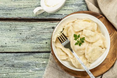 Hamur köftesi ya da süzme peynirli ve ekşi kremalı Vareniki. Geleneksel Doğu Avrupa mutfağı. Çatal bıçak, köy tarzı, tahta tahta arka plan, üst manzara.