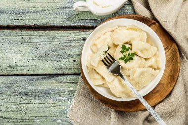 Hamur köftesi ya da süzme peynirli ve ekşi kremalı Vareniki. Geleneksel Doğu Avrupa mutfağı. Çatal bıçak, köy tarzı, tahta tahta arka plan, üst manzara.