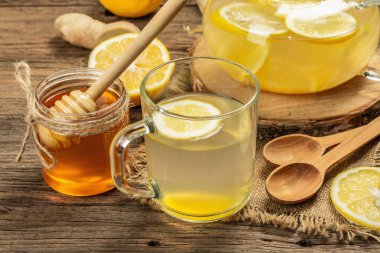 Tahta arka planda cam bir fincanda limonlu ve ballı sıcak zencefil çayı. Alternatif tıp, soğuk algınlığı ve grip için doğal ev tedavisi.
