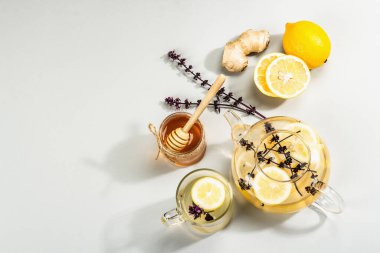 Açık gri arka planda cam bir fincanda limonlu ve ballı sıcak zencefil çayı. Alternatif tıp, soğuk algınlığı ve grip için doğal ev tedavisi, modern sert ışık, karanlık gölge, üst görüş