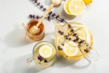 Açık gri arka planda cam bir fincanda limonlu ve ballı sıcak zencefil çayı. Alternatif tıp, soğuk algınlığı ve grip için doğal ev tedavisi, modern sert ışık, karanlık gölge, üst görüş