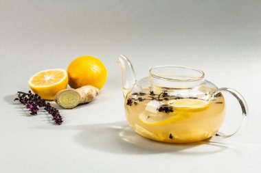 Açık gri arka planda cam bir fincanda limonlu ve ballı sıcak zencefil çayı. Alternatif tıp, soğuk algınlığı ve grip için doğal ev tedavisi, modern sert ışık, karanlık gölge, kopyalama alanı