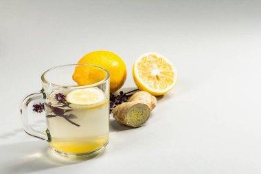 Açık gri arka planda cam bir fincanda limonlu ve ballı sıcak zencefil çayı. Alternatif tıp, soğuk algınlığı ve grip için doğal ev tedavisi, modern sert ışık, karanlık gölge, kopyalama alanı