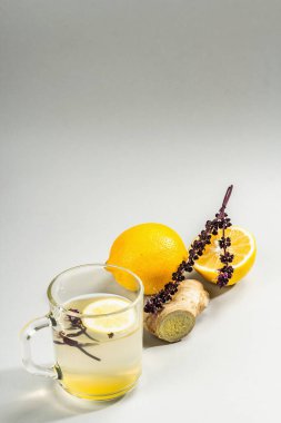 Açık gri arka planda cam bir fincanda limonlu ve ballı sıcak zencefil çayı. Alternatif tıp, soğuk algınlığı ve grip için doğal ev tedavisi, modern sert ışık, karanlık gölge, kopyalama alanı