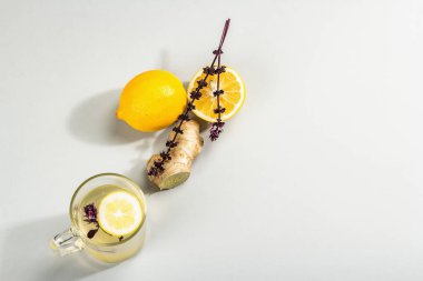 Açık gri arka planda cam bir fincanda limonlu ve ballı sıcak zencefil çayı. Alternatif tıp, soğuk algınlığı ve grip için doğal ev tedavisi, modern sert ışık, karanlık gölge, üst görüş