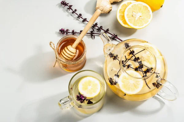 Açık gri arka planda cam bir fincanda limonlu ve ballı sıcak zencefil çayı. Alternatif tıp, soğuk algınlığı ve grip için doğal ev tedavisi, modern sert ışık, karanlık gölge, üst görüş