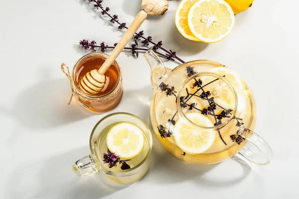 Açık gri arka planda cam bir fincanda limonlu ve ballı sıcak zencefil çayı. Alternatif tıp, soğuk algınlığı ve grip için doğal ev tedavisi, modern sert ışık, karanlık gölge, üst görüş