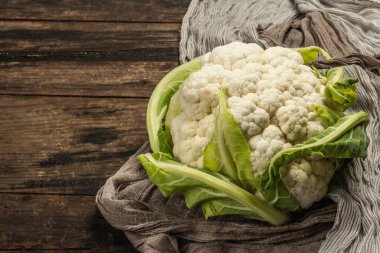 Seramik bir kasede yeşil yaprakları olan güzel karnabahar. Eski peçete, eski ahşap masa, kopyalama alanı