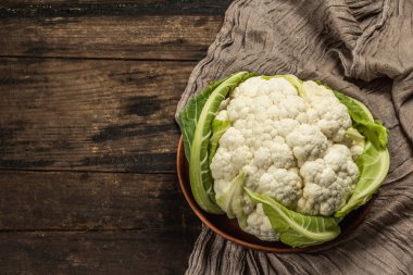 Seramik bir kasede yeşil yaprakları olan güzel karnabahar. Eski peçete, eski ahşap masa, üst manzara.