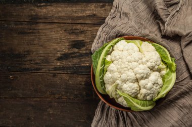 Seramik bir kasede yeşil yaprakları olan güzel karnabahar. Eski peçete, eski ahşap masa, üst manzara.