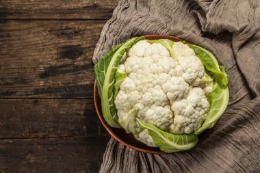 Seramik bir kasede yeşil yaprakları olan güzel karnabahar. Eski peçete, eski ahşap masa, üst manzara.