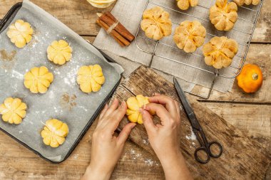 Balkabağı çörekleri ya da bisküviler, geleneksel sonbahar pişmiş ürünler. Kadın eli kurabiye yapıyor. Mevsimlik ev yapımı yemekler ve sonbahar dekorasyonu. Eski tahta arka plan, üst görünüm