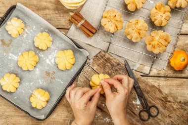 Balkabağı çörekleri ya da bisküviler, geleneksel sonbahar pişmiş ürünler. Kadın eli kurabiye yapıyor. Mevsimlik ev yapımı yemekler ve sonbahar dekorasyonu. Eski tahta arka plan, üst görünüm