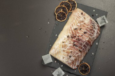 Çiğ pollock (Pollachius virens) fileto. Donmuş balık sağlıklı besin yaşam tarzı için. Kuru limon dilimleri, deniz tuzu, biber, buz. Siyah taş arkaplan, üst görünüm