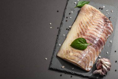 Çiğ pollock (Pollachius virens) fileto. Sağlıklı yaşam tarzı için taze balık. Sarımsak, deniz tuzu, biber, yeşillik. Siyah taş arkaplan, üst görünüm