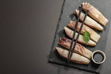 Çiğ pollock (Pollachius virens) parçaları. Sağlıklı yaşam tarzı için taze balık. Deniz tuzu, yeşillik, soya sosu, yemek çubukları. Siyah taş arkaplan, üst görünüm