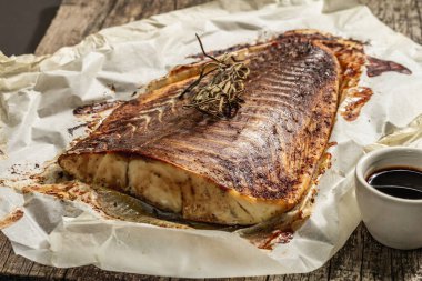 Fırında Pollock (Pollachius virens) fileto. Sağlıklı yaşam tarzı için teriyaki soslu balık. Biberiye, soya sosu, parşömen. Ahşap durak, siyah taş beton arka plan, yakın plan.