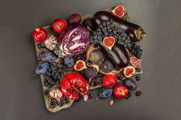 Blue, red and purple food. Culinary background of fruits and vegetables. Fresh figs, plums, onions, eggplant, grapes, cabbage, apples, garlic, dogwood, pomegranate. Black stone background, flat lay