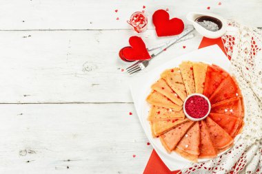 İnce kırmızı krep ya da ahududu şekerli krep ve tatlı kalpli hamur işi. Sevgililer Günü ya da Anneler Günü için romantik bir kahvaltı. Kademeli kırmızı yemek, beyaz ahşap arka plan, üst görünüm