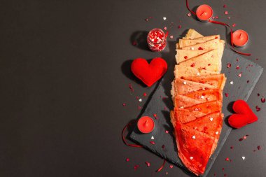 Romantik kahvaltı fikri, kırmızı krep ya da tatlı kalpler üzerine ince krepler. Sevgililer Günü ya da Anneler Günü için kutlama yemeği. Modaya uygun sert ışık, karanlık gölge. Siyah taş arkaplan, üst görünüm