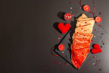 Romantik kahvaltı fikri, kırmızı krep ya da tatlı kalpler üzerine ince krepler. Sevgililer Günü ya da Anneler Günü için kutlama yemeği. Modaya uygun sert ışık, karanlık gölge. Siyah taş arkaplan, üst görünüm