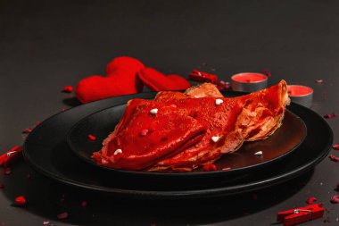 Romantik kahvaltı fikri, kırmızı krep ya da tatlı kalpler üzerine ince krepler. Sevgililer Günü ya da Anneler Günü için kutlama yemeği. Modaya uygun sert ışık, karanlık gölge. Siyah taş beton arka plan, kapat
