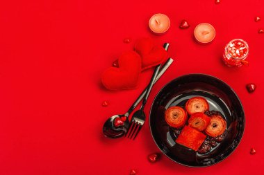 Romantik kahvaltı fikri, kırmızı krep ya da tatlı kalpler üzerine ince krepler. Sevgililer Günü ya da Anneler Günü için kutlama yemeği. Çilek reçeli, çatal bıçak takımı, parlak kırmızı arka plan, üst manzara.